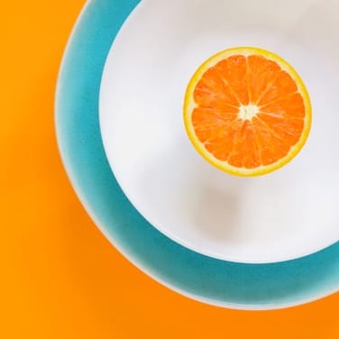 a cut orange placed in a white bowl on blue plate against an orange background